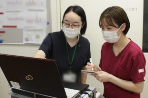 2.PCの前でメンバーと情報共有している看護師の写真