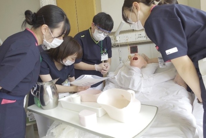 ベッドの上に人体模型を置き4人の新人看護師が口腔ケアの研修をしている